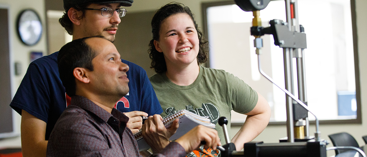 Professor and two students utilizing engineering equipment