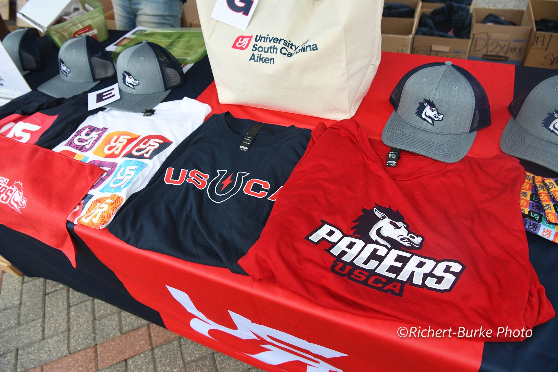 T-shirts, hats, and stickers with the USCA logo on a table.